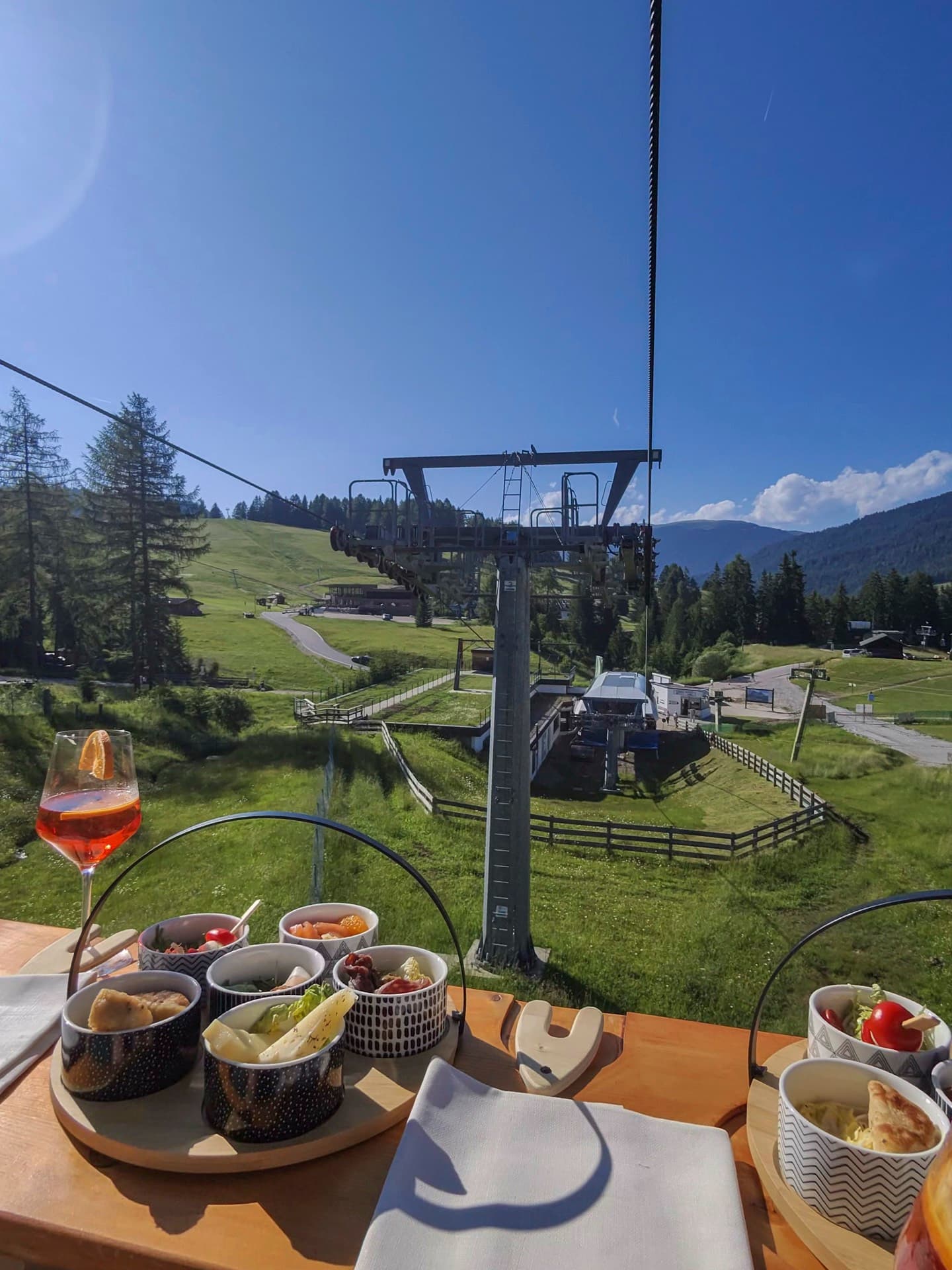 The Mont de Sëura chairlift climbing over green meadows toward the larch wood.