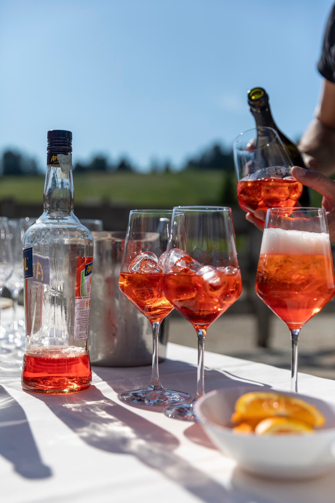 The barman pouring prosecco into a row of spritz glasses in the sun.