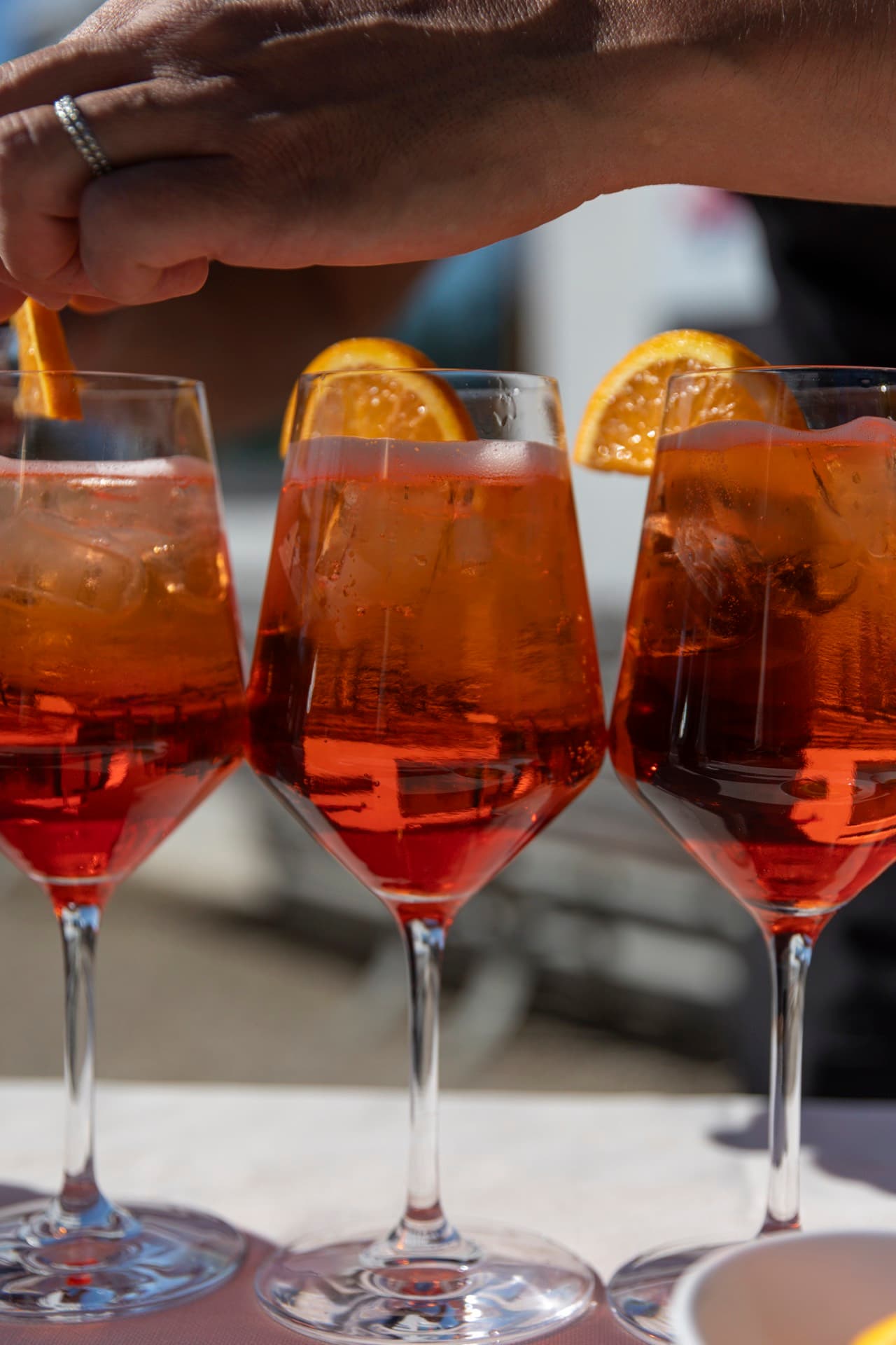 Three spritz glasses garnished with orange, ready on the departure table.